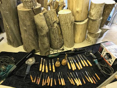 Wood carving tools in front of logs for sculpture project